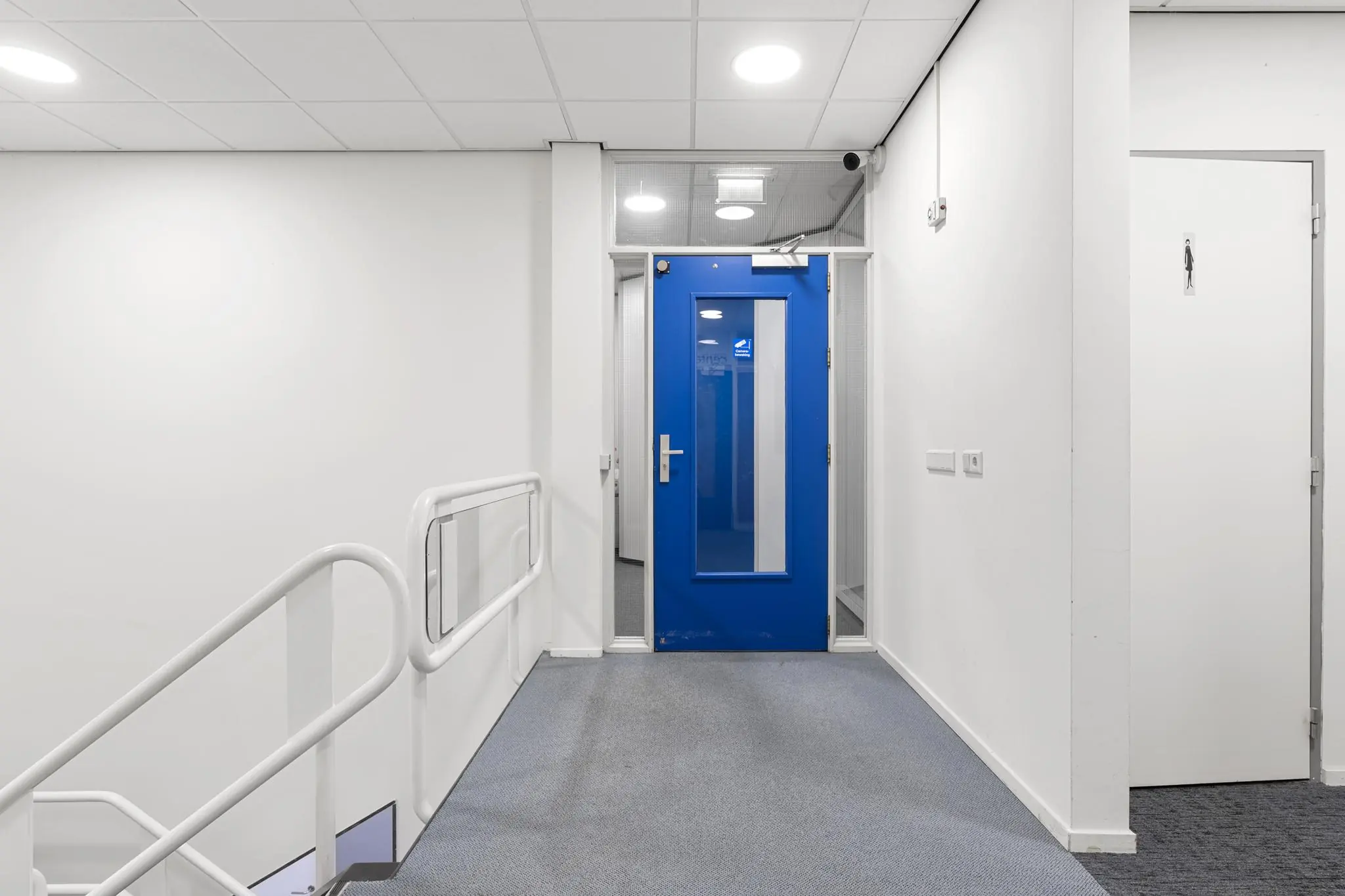 Hal met trap, blauwe deur en deur naar toiletruimte in een kantoorpand aan de Huis-ter-Heideweg.